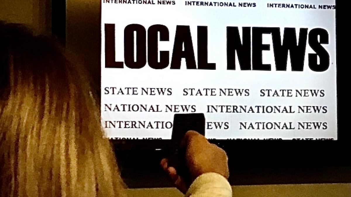 child holds remote control in front of television screen featuring the words "local news"
