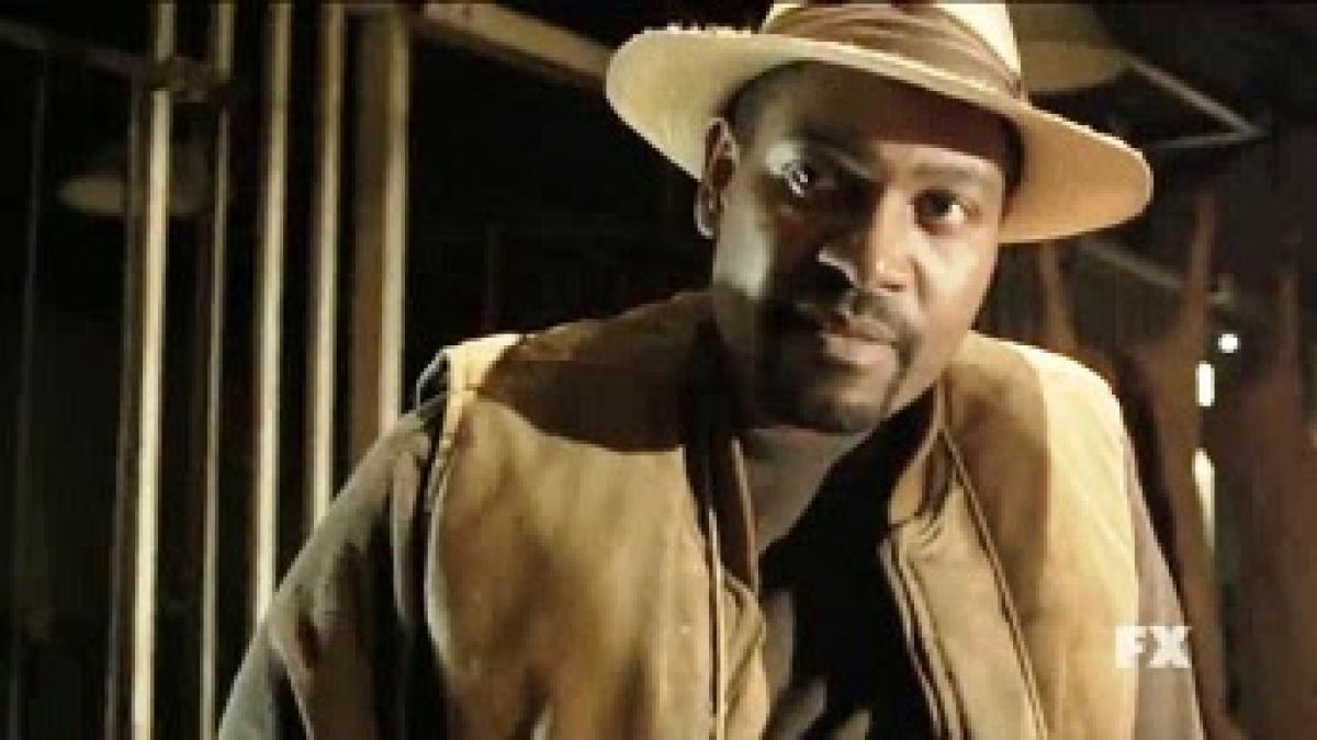 actor Mykelti Williamson as Ellstin Limehouse in FX series Justified, a Black man in a barn wearing a straw hat and work vest