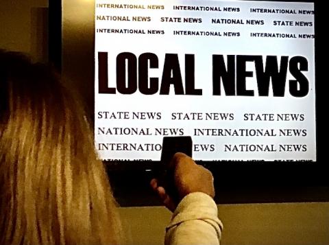 child holds remote control in front of television screen featuring the words "local news"